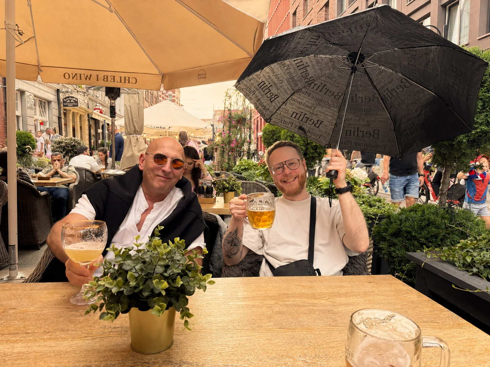 Zwei Kollegen prosten sich unter einem Regenschirm zu